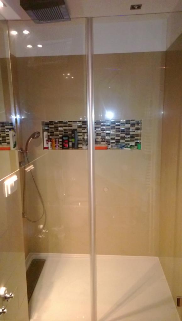 Nowoczesna kabina prysznicowa z wnęką wyłożoną mozaiką, widok z zewnątrz, beżowe ściany, biały brodzik, deszczownica, oświetlenie punktowe.