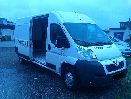 Biały Peugeot Boxer z otwartymi drzwiami bocznymi, widoczne aluminiowe wnętrze paki, zaparkowany na zewnątrz w pochmurny dzień.