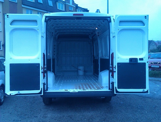 Wnętrze paki białego busa z otwartymi drzwiami, przygotowanego do transportu, widok z tyłu w Słupsku.
