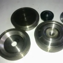 Metalowe elementy obrobione w Słupsku, widoczne ślady po toczeniu i frezowaniu, różne kształty i rozmiary, leżące na białym tle.