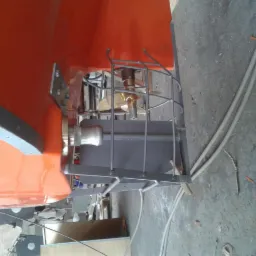 Pomarańczowy kadłub łodzi z widocznym, osłoniętym metalową klatką, mosiężnym śmigłem i wałem napędowym. Widoczne ślady obróbki i montażu.