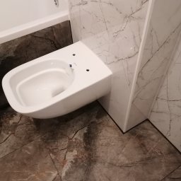 CENTRUM USŁUG - DANIEL NOŻEWSKI - Wisząca miska WC Rimfree zamontowana w łazience w Świnoujściu, obok wanna z marmurowym wykończeniem, na podłodze i ścianach gres 60x120 cm imitujący marmur.