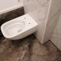 Wisząca miska WC Rimfree zamontowana w łazience w Świnoujściu, obok wanna z marmurowym wykończeniem, na podłodze i ścianach gres 60x120 cm imitujący marmur.