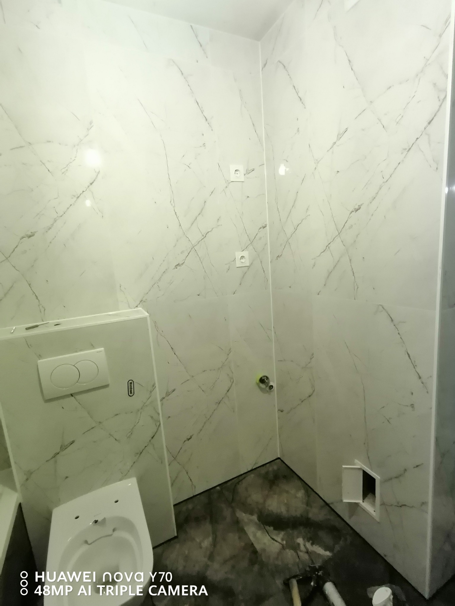 Wykończona łazienka w Świnoujściu z płytkami gresowymi 60x120 cm imitującymi marmur na ścianach, podwieszany sedes z zabudową, widoczny fragment podłogi z ciemnymi płytkami i otwarty rewizyjny właz.