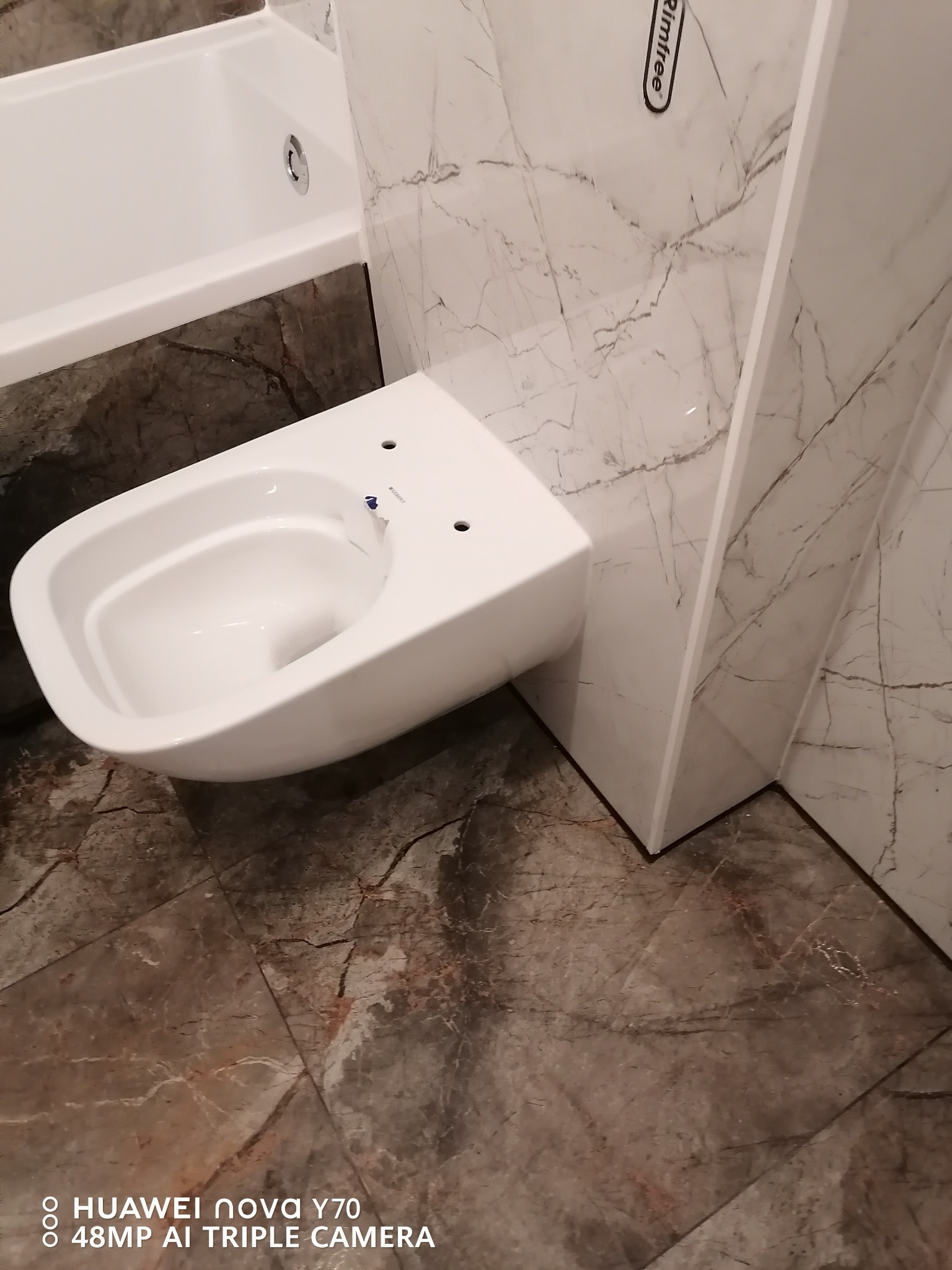 Wisząca miska WC Rimfree zamontowana w łazience w Świnoujściu, obok wanna z marmurowym wykończeniem, na podłodze i ścianach gres 60x120 cm imitujący marmur.