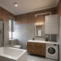 Projektowanie Wnętrz Katarzyna Ćwiek - Nowoczesna łazienka z ceglaną ścianą, szarą glazurą i drewnianą szafką pod umywalką. Widoczna wanna, toaleta i pralka. Oświetlenie LED nad lustrem.