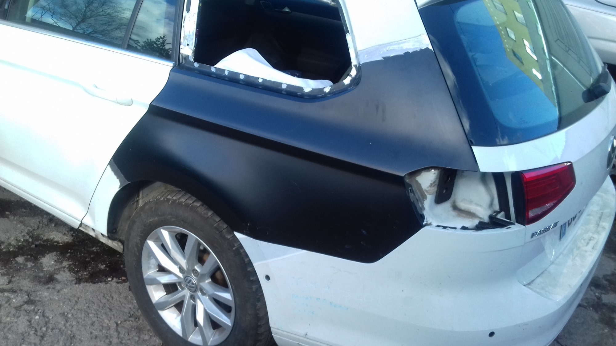 Biały VW Passat kombi z uszkodzonym tyłem, w trakcie naprawy blacharskiej, z elementami pokrytymi czarnym podkładem przed lakierowaniem.