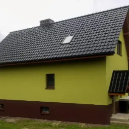 Dom jednorodzinny z ocieploną elewacją w kolorze oliwkowym i brązowym cokołem, czarny dach z dachówką ceramiczną i oknem dachowym