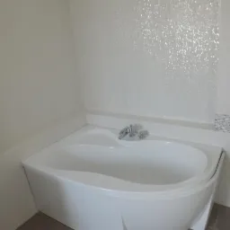 Biała, narożna wanna z chromowaną armaturą na tle ściany wyłożonej błyszczącą mozaiką. Detale wykończenia łazienki z subtelnymi akcentami dekoracyjnymi.