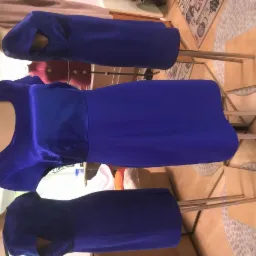 Trzy niebieskie sukienki na manekinach krawieckich, środkowa z błyszczącego materiału, widoczne elementy wyposażenia pracowni krawieckiej w tle.