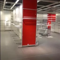 Metalowy regał sklepowy z czerwonymi panelami w Zabrzu, widok z perspektywy podłogi, oświetlenie sufitowe, puste półki w tle.