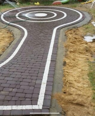 Nowa ścieżka z kostki brukowej w kształcie klucza z okrągłym placem, czyszczona wodą pod ciśnieniem, obrzeża z betonu, piasek po bokach.