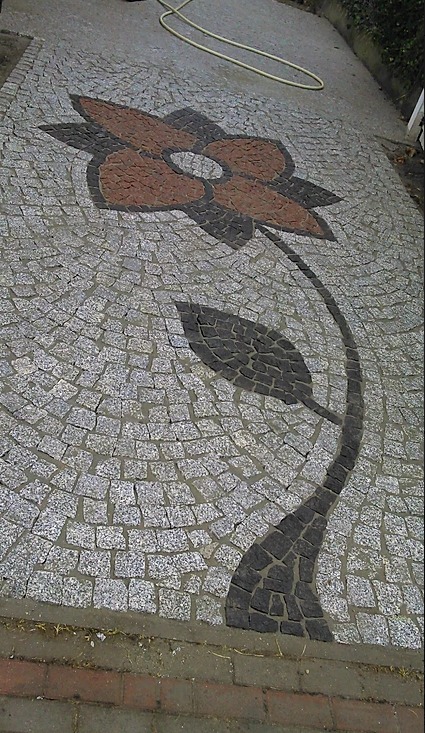 Dekoracyjny wzór kwiatowy z kostki granitowej w odcieniach szarości, brązu i czerni, tworzący unikalną kompozycję na chodniku.