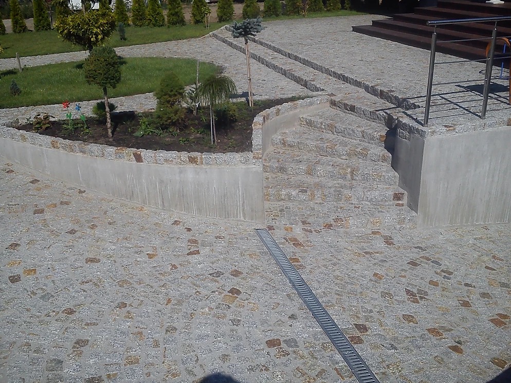 Ułożona kostka granitowa w Koninie tworząca ścieżkę, schody i obrzeże rabaty kwiatowej z widocznym odpływem liniowym.