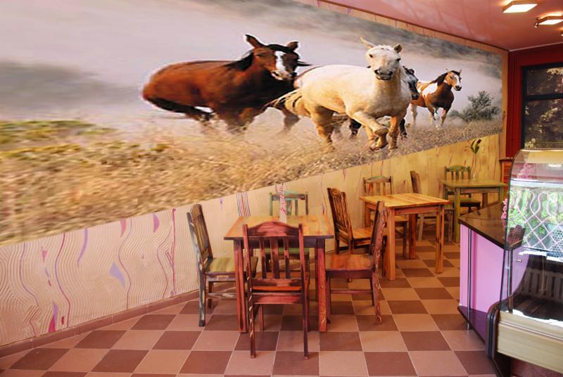 Wnętrze kawiarni z fototapetą przedstawiającą galopujące konie, drewniane stoły i krzesła.