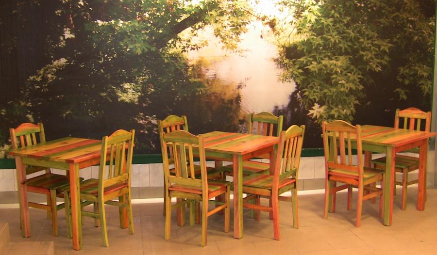 Aranżacja wnętrza z trzema zestawami stołów i krzeseł pomalowanych w paski na pomarańczowo i zielono, na tle fototapety z motywem leśnym.