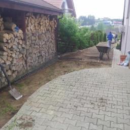 Ogrody-Rydz Zakładanie I Pielęgnacja Zieleni - Przygotowanie terenu pod ogród: wyrównana ziemia, taczka z ziemią, grabie, szpadel, drewno na opał. Prace ogrodowe w toku, widok z boku.