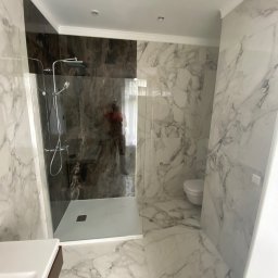 MTM rem-bud - Wykończona łazienka z kabiną typu walk-in, marmurowymi płytkami na ścianach i podłodze, oraz toaletą w rogu. Widoczna armatura w odcieniach srebra i brązu.