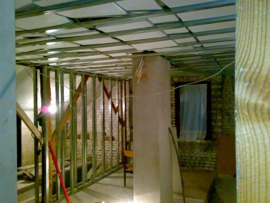 Konstrukcja metalowa pod zabudowę z płyt gipsowo-kartonowych na suficie i ścianach w trakcie montażu, widoczne elementy ocieplenia, surowy stan pomieszczenia z ceglanymi ścianami w tle.