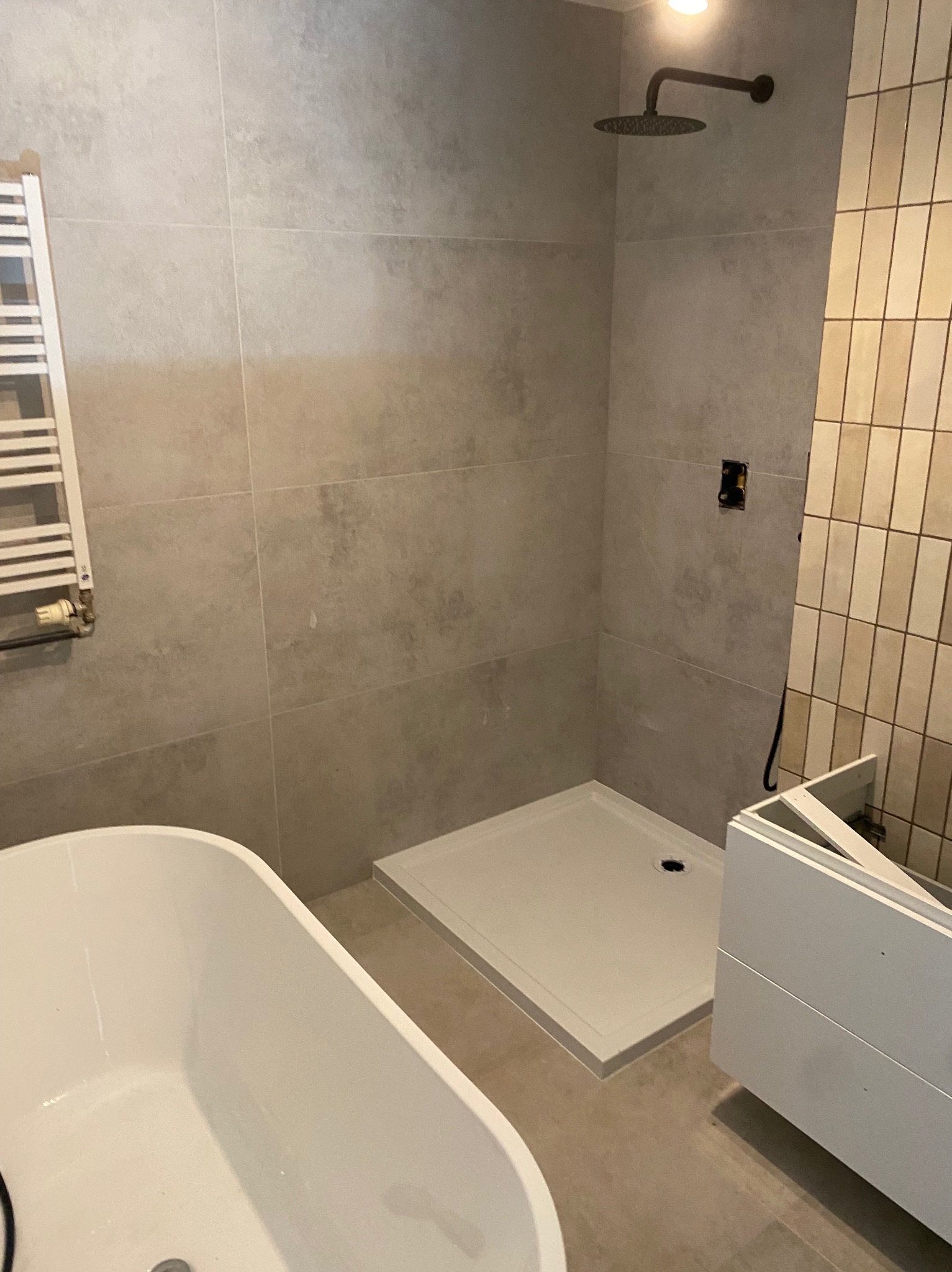 Nowoczesna łazienka w trakcie wykańczania: biała wanna wolnostojąca, brodzik, grzejnik drabinkowy i częściowo zamontowana szafka pod umywalkę.