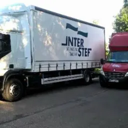 Biała ciężarówka Iveco z naczepą i czerwony bus Renault Master zaparkowane obok siebie na asfaltowej drodze, widoczne logo firmy transportowej 'INTER STEF' na naczepie.