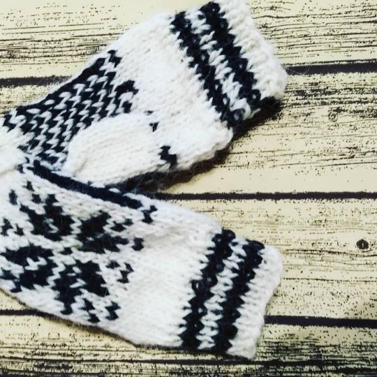 Para białych, dzierganych rękawic z czarnym wzorem na drewnianym tle, uchwycona z bliska, prezentująca detale splotu.