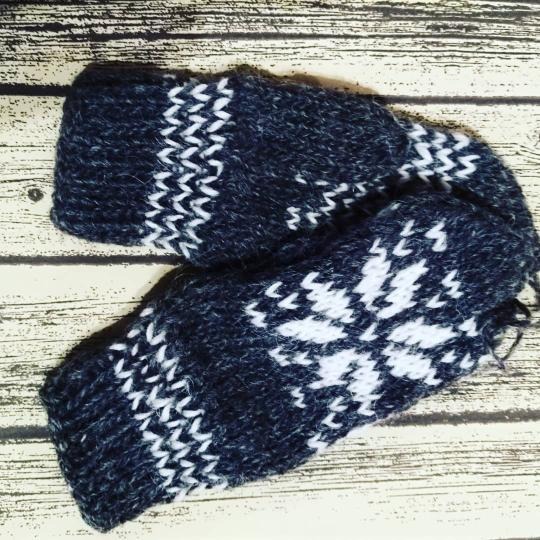 Granatowe rękawiczki bez palców z białym wzorem śnieżynek i zygzaków leżą na drewnianym tle.