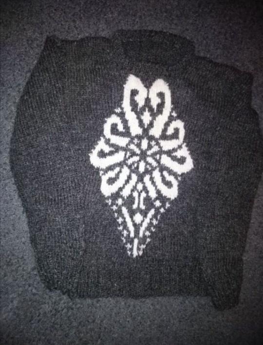 Ciemnoszary, ręcznie robiony sweter z białym, geometrycznym wzorem kwiatowym na środku.