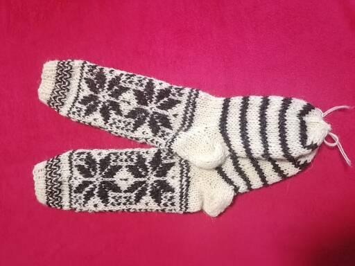 Para ręcznie robionych, wełnianych skarpet z wzorem śnieżynek i pasków, leżąca na różowym tle.