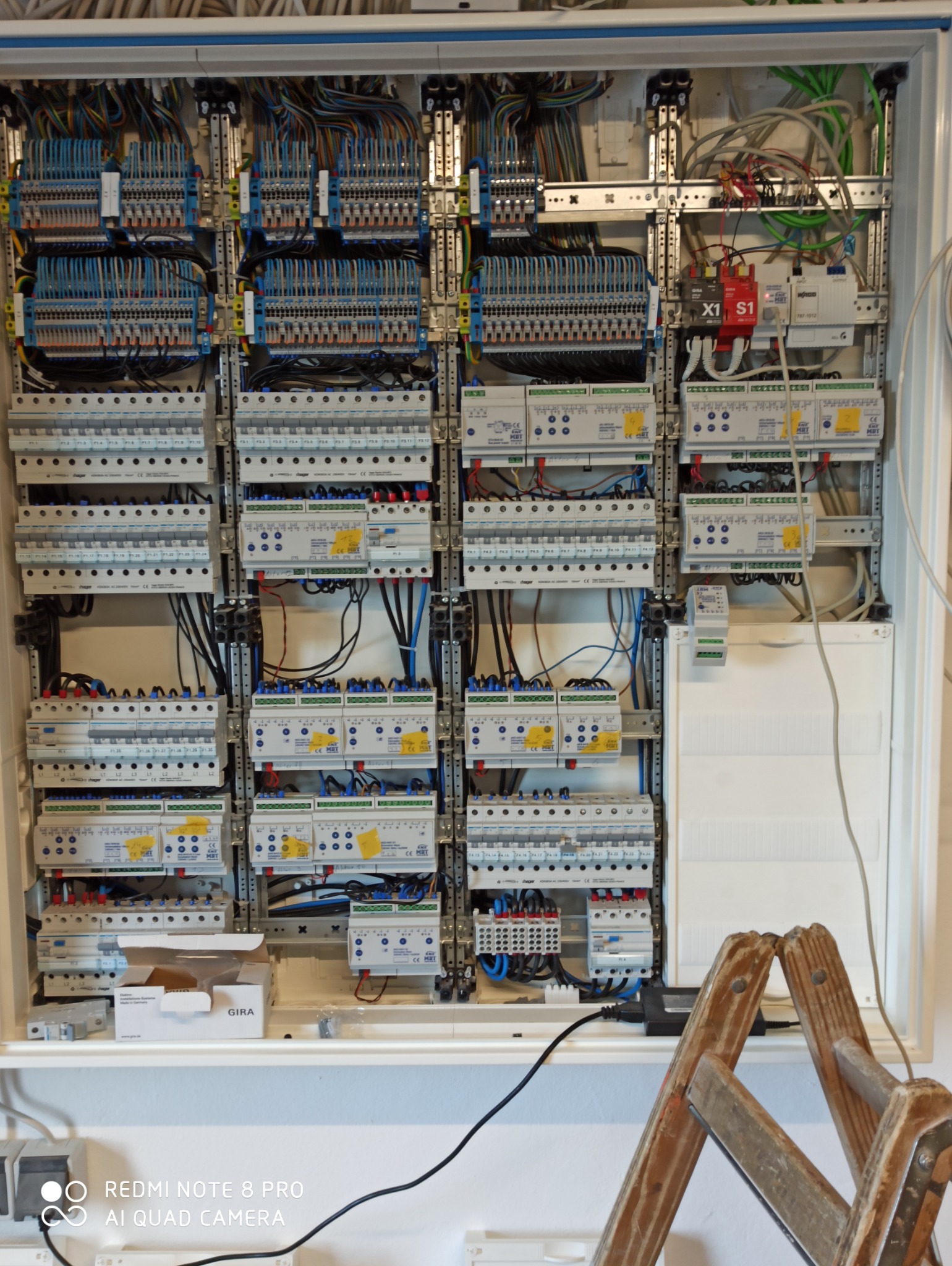 Rozbudowana skrzynka elektryczna z licznymi bezpiecznikami, przekaźnikami i okablowaniem, widoczna drabina drewniana w dolnym rogu.