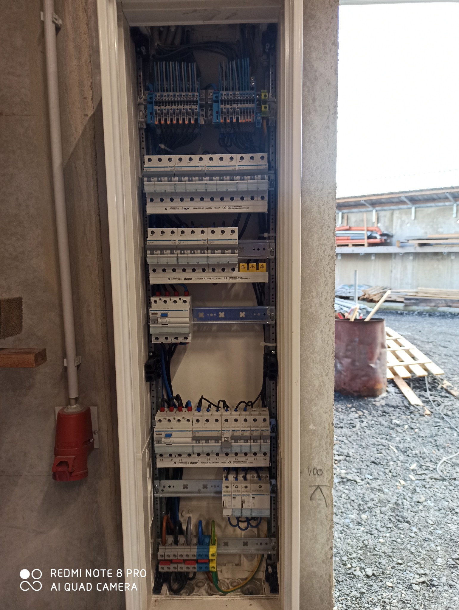 Rozdzielnica elektryczna z zabezpieczeniami i przewodami w obudowie, widoczna instalacja na zewnątrz budynku w trakcie budowy.