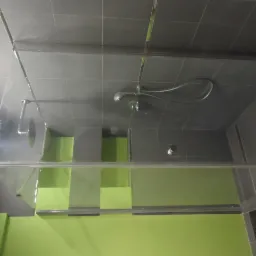 Nowoczesna kabina prysznicowa z szarymi płytkami i zielonym akcentem kolorystycznym. Widoczne detale armatury i szklane elementy kabiny.