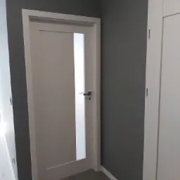 Nowoczesne wnętrze: Szara ściana, białe drzwi z matowym szkłem i szara podłoga z płytek.