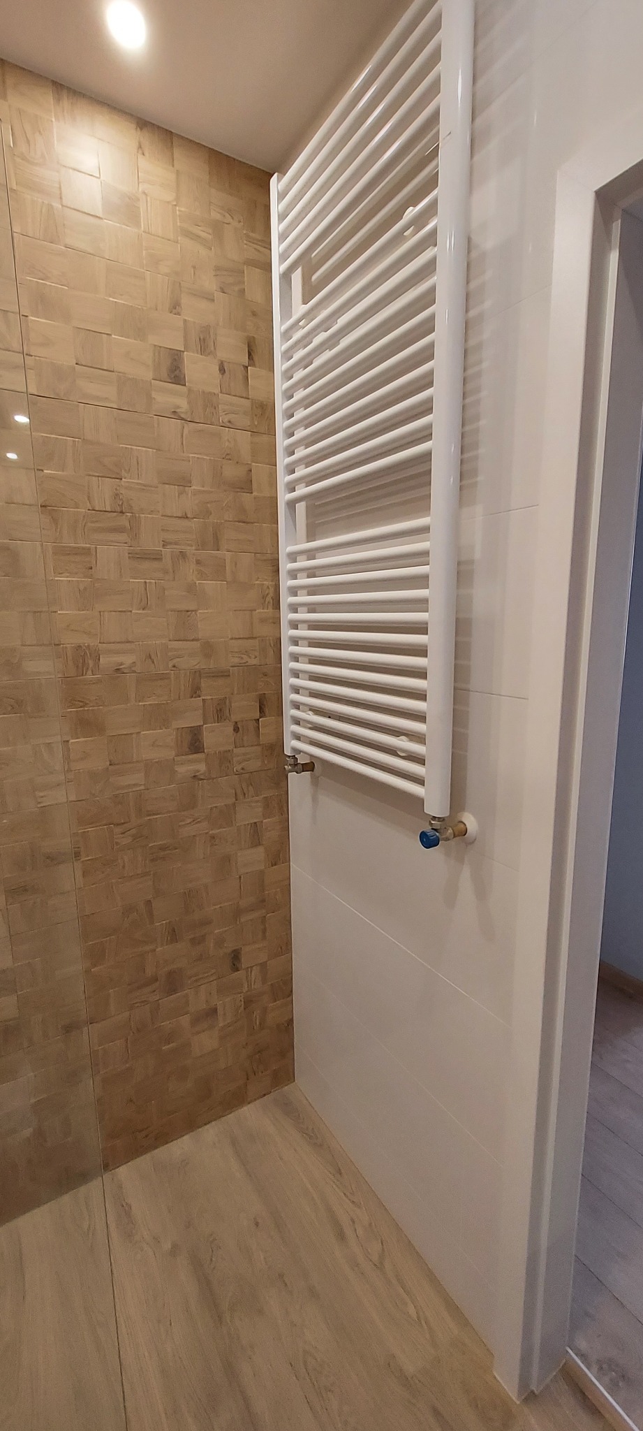 Nowoczesna łazienka z drewnopodobnymi płytkami na ścianie, białym grzejnikiem drabinkowym i podłogą imitującą drewno.