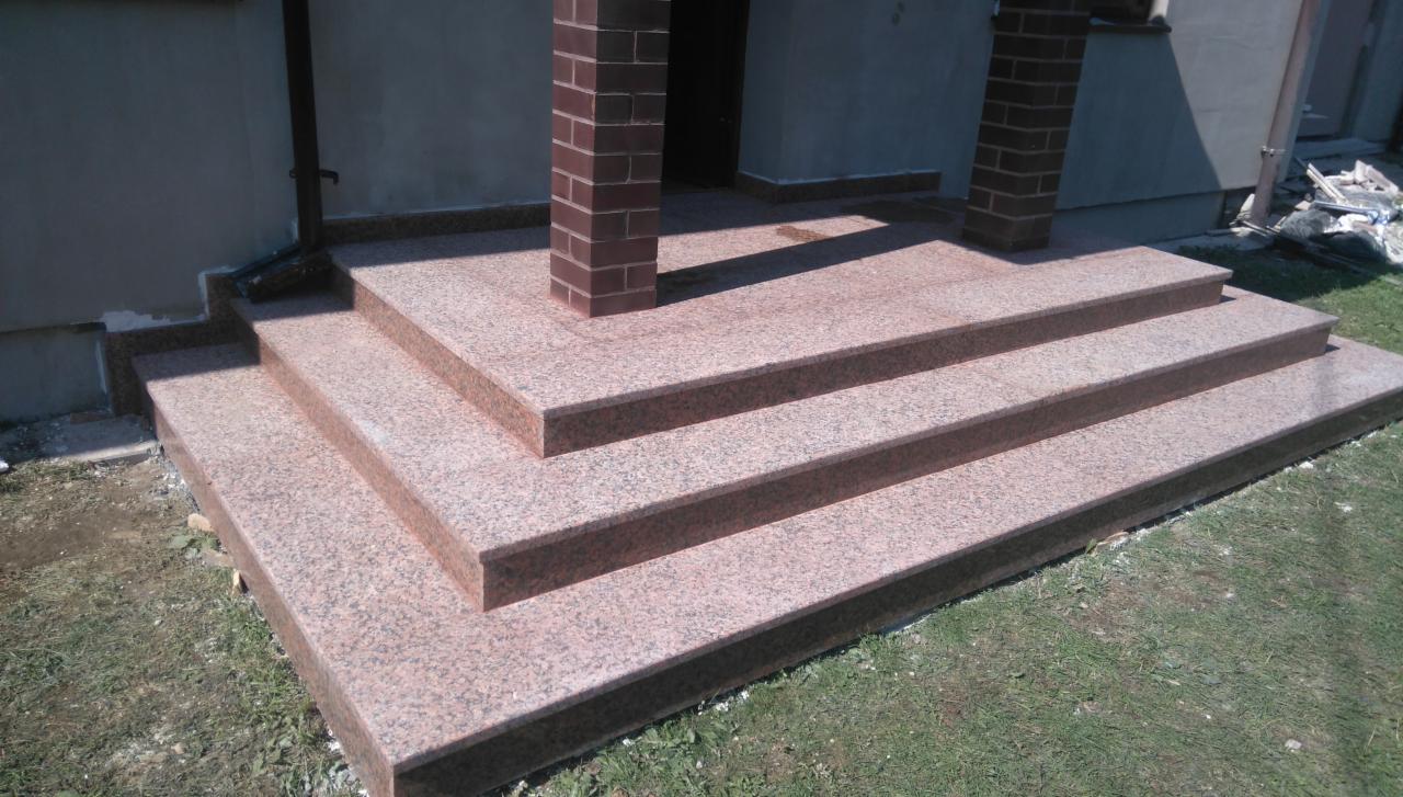 Granitowe schody wejściowe z dwoma ceglanymi filarami, prowadzące do domu, z widocznym fragmentem trawnika