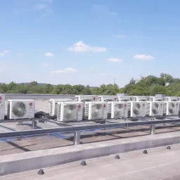 Rząd jednostek zewnętrznych klimatyzacji LG Inverter V, zainstalowanych na dachu budynku w Pogórzu, z widokiem na zalesione wzgórza w tle.