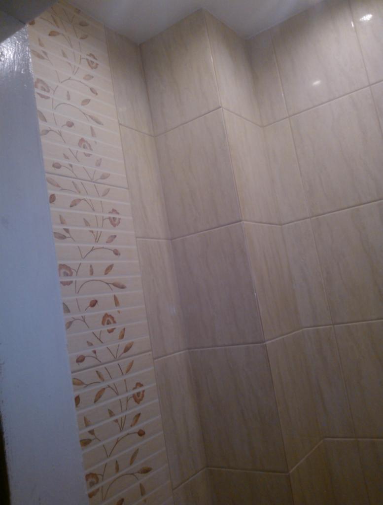 Wykończona łazienka z beżowymi płytkami, dekoracyjny pas z motywem kwiatowym, widok na narożnik pomieszczenia.