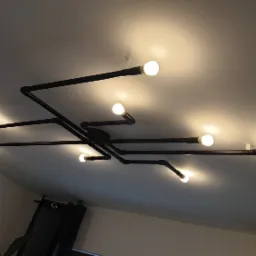 Industrialna lampa sufitowa z czarnych rur i ośmiu żarówek o ciepłej barwie, zamontowana na białym suficie w nowoczesnym wnętrzu.