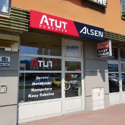 Fasada budynku z szyldami firm: Atut Komputer (serwis notebooków, komputerów, kas fiskalnych), Alsen, Insert programy dla firm, Serwis Komputery Kasy Fiskalne, Budvar Centrum okna z niewidocznym...
