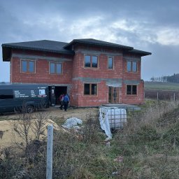 P.P.H.U. STOLAR SYSTEM ŁUKASZ ZIÓŁKOWSKI - Budowa domu w stanie surowym otwartym z zamontowanymi oknami. Na pierwszym planie bus firmy montującej okna. Pochmurne niebo.