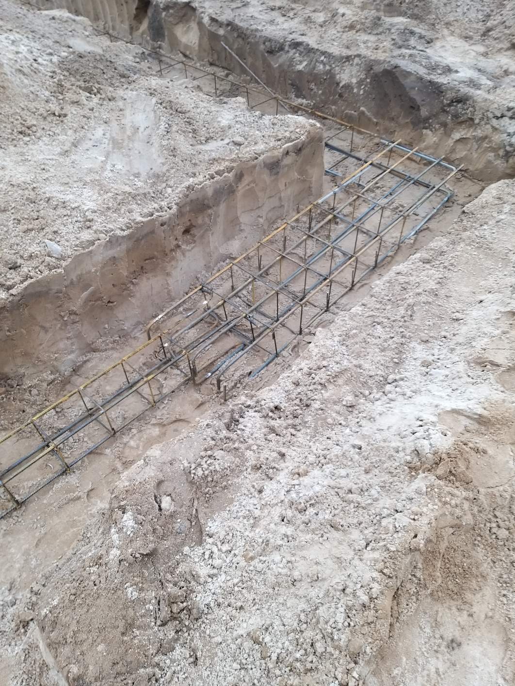 Zbrojenie stalowe w wykopie fundamentowym, przygotowane do zalania betonem; widoczne ślady ziemi na konstrukcji.