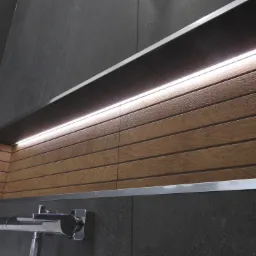 Narożna półka w kabinie prysznicowej wyłożona drewnopodobnymi panelami z oświetleniem LED, ciemnoszare płytki na ścianach, chromowana bateria.