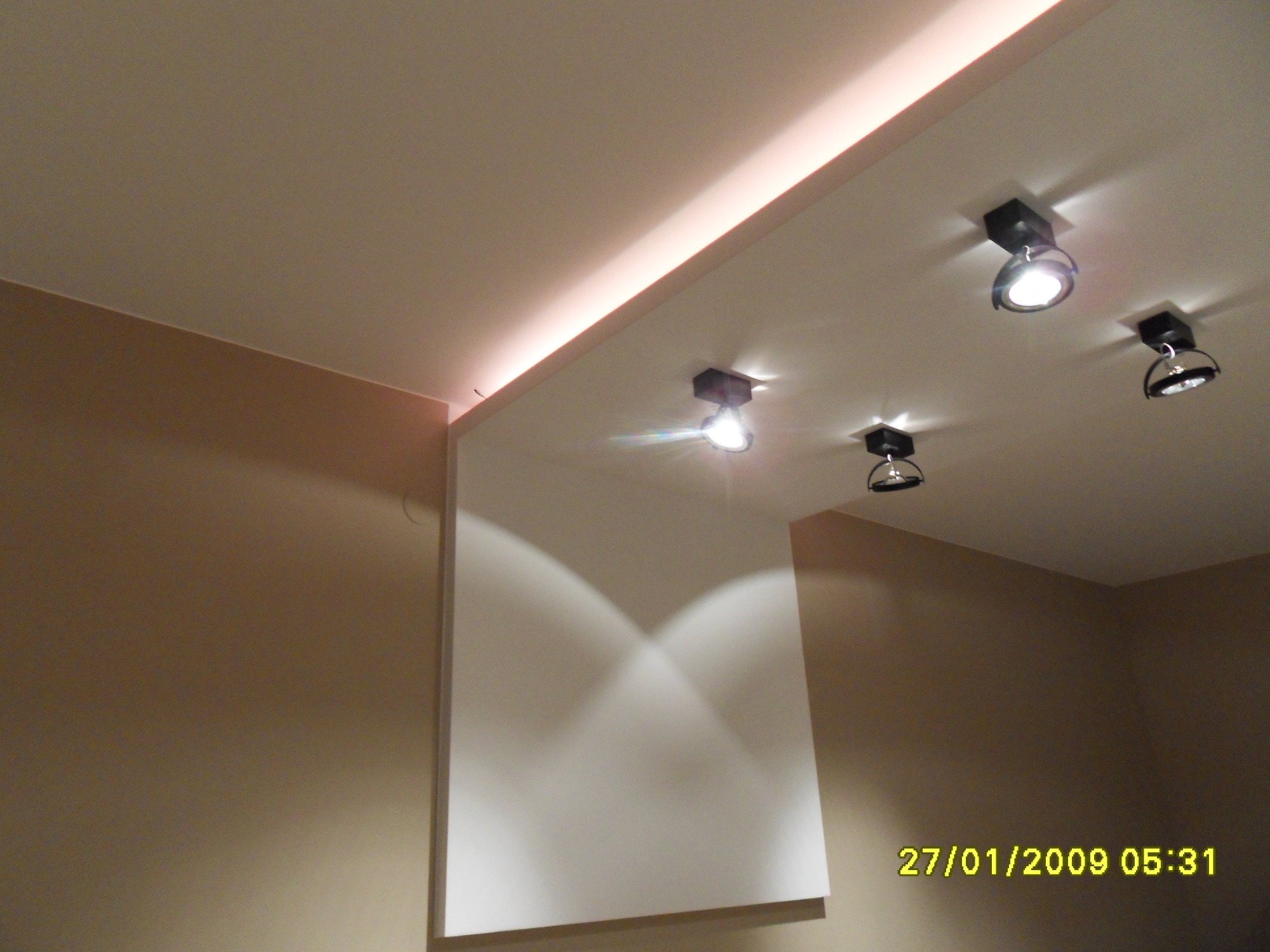 Oświetlenie sufitowe z czterema reflektorami halogenowymi i listwą LED w narożniku, ściany w kolorze beżowym.