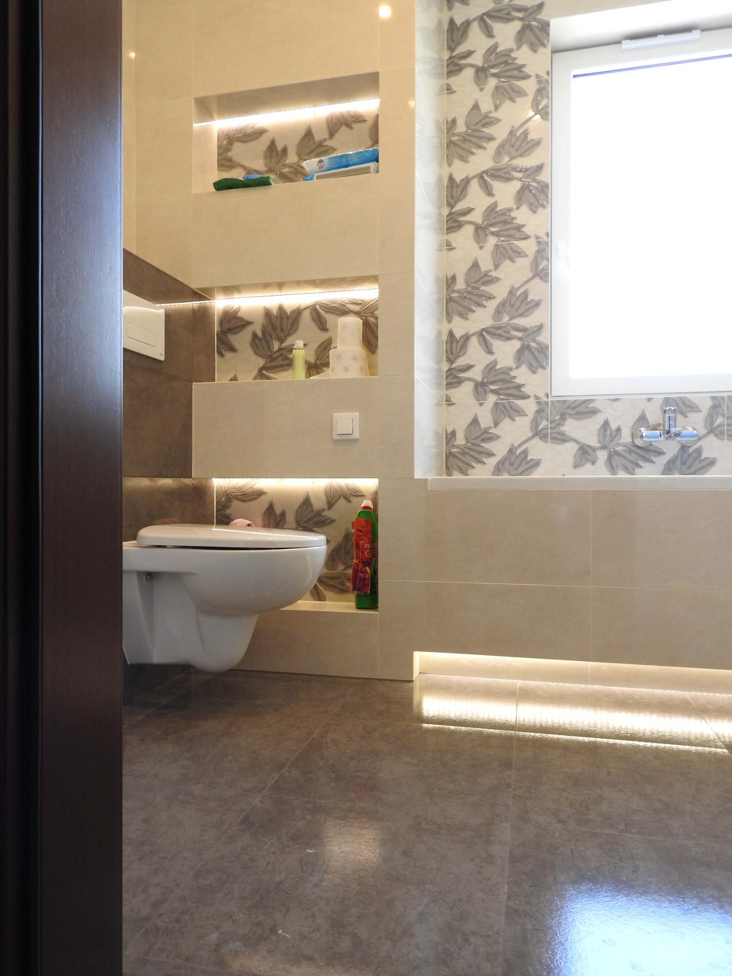 Wykończona łazienka w Łodzi z podświetlanymi półkami i płytkami w liście, widoczna toaleta i fragment podłogi.