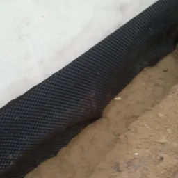 Przygotowanie wykopu przy fundamencie budynku, zabezpieczonego czarną, karbowaną folią hydroizolacyjną, zasypywanego piaskiem.