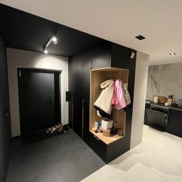 P.P.U.H Dariusz Rogowiec - Nowoczesny przedpokój z czarną zabudową szafy wnękowej z otwartą półką na ubrania i akcesoria, widoczna część kuchni w tle.