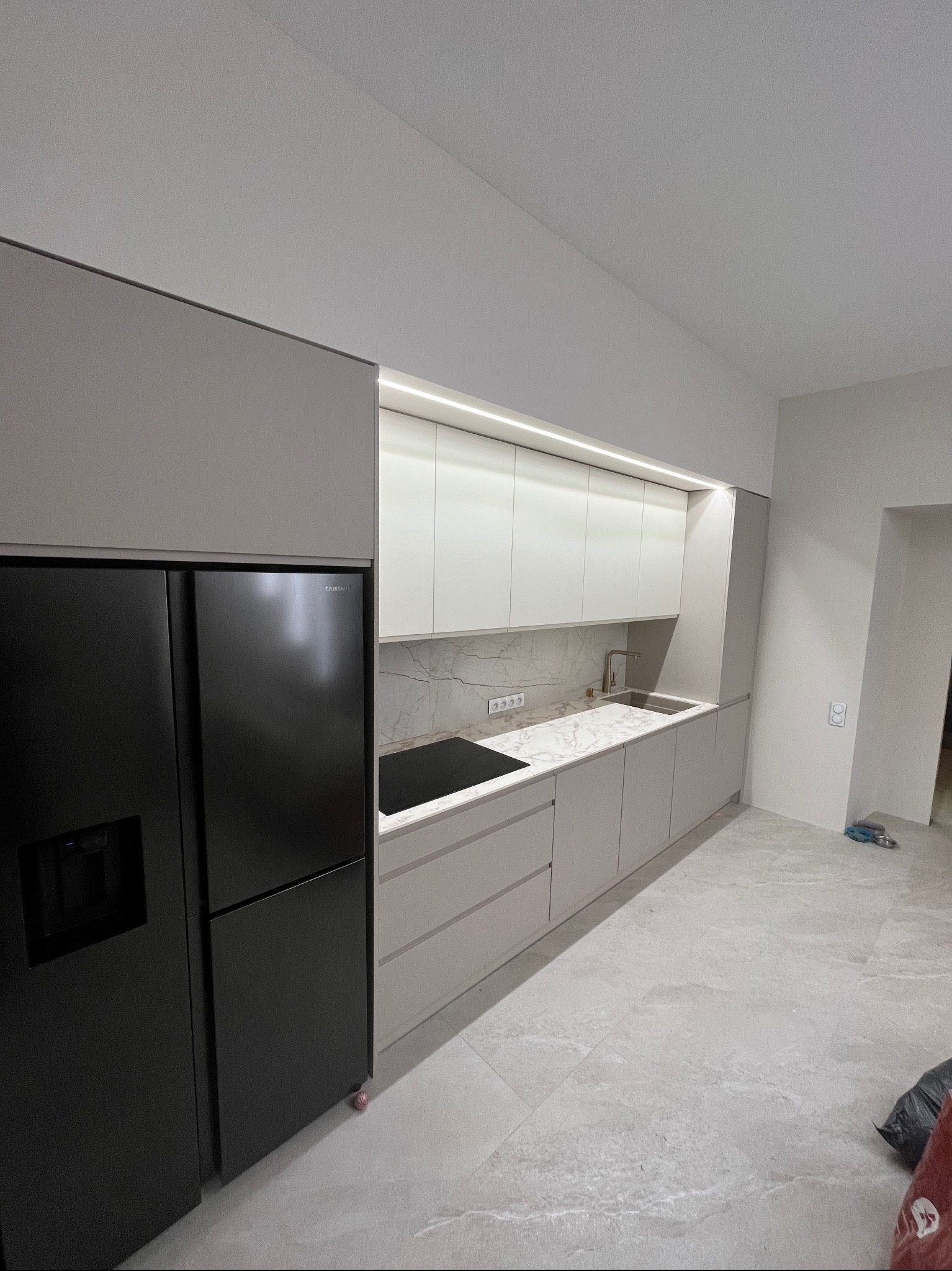Nowoczesna kuchnia z szarymi frontami szafek, czarną lodówką Samsung i blatem imitującym marmur, oświetlenie LED pod szafkami górnymi.