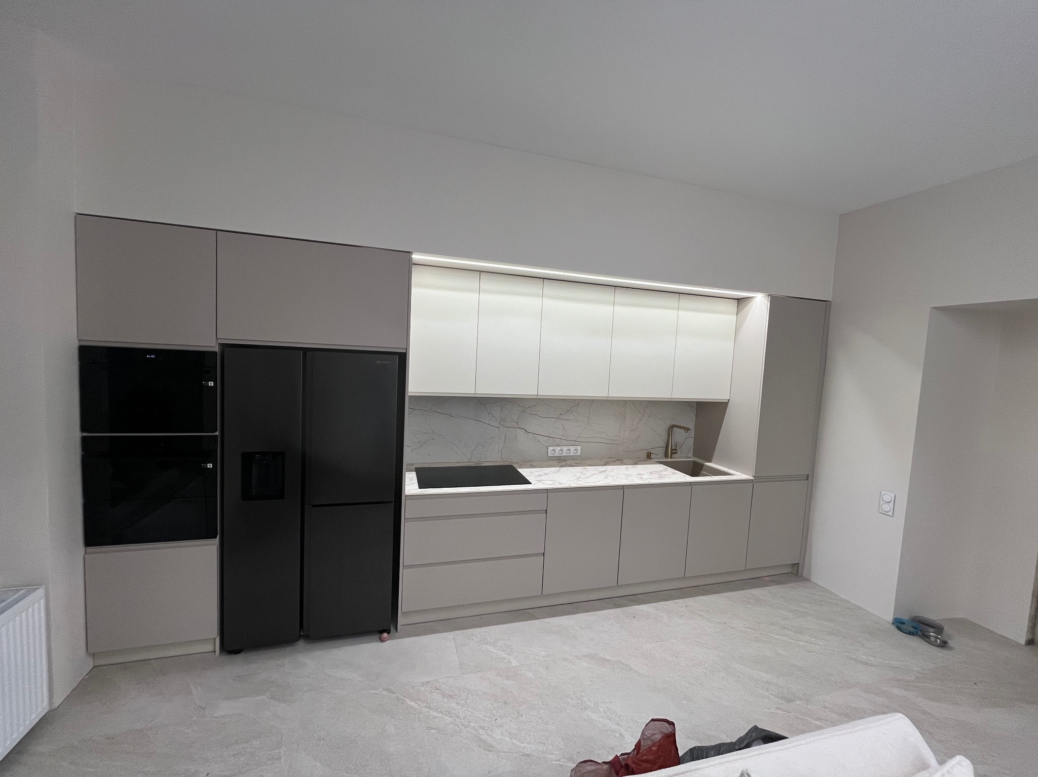 Nowoczesna kuchnia z zabudową w odcieniach szarości i bieli, z czarną lodówką i piekarnikiem, marmurowy backsplash, oświetlenie LED podszafkowe.