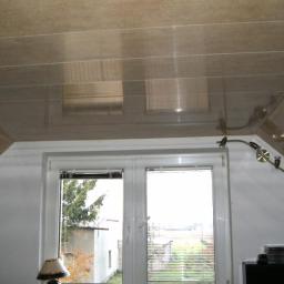 REM- KOS Rafał Pieńkos Usługi Remontowo -Budowlane - Błyszczący, beżowy sufit napinany z widocznymi liniami łączeń, zamontowany w pokoju na poddaszu z oknem i lampą na ścianie.