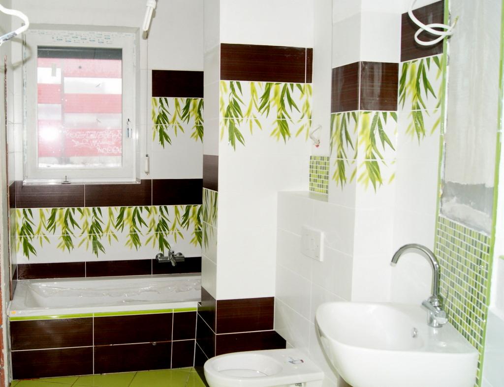 Ukończona łazienka z brązowymi i białymi płytkami z motywem bambusa, zielona podłoga, biała umywalka i wanna zabezpieczona folią, widoczne niedokończone fragmenty mozaiki.